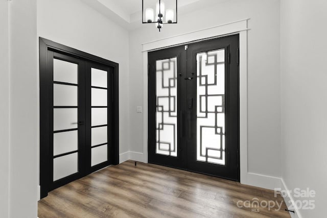 foyer entrance featuring baseboards, an inviting chandelier, french doors, and wood finished floors