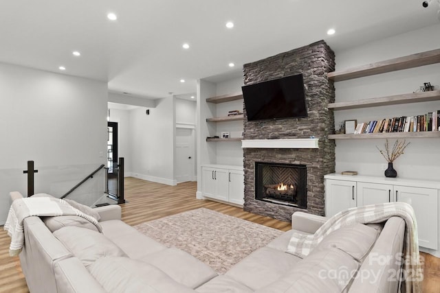 living area with recessed lighting, baseboards, light wood finished floors, and a stone fireplace