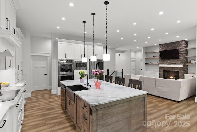 kitchen featuring a kitchen island with sink, light wood-type flooring, recessed lighting, a sink, and appliances with stainless steel finishes