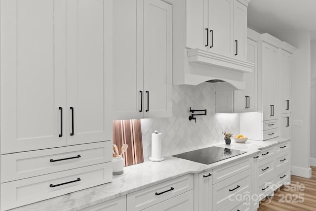 kitchen with light stone counters, light wood-style floors, black electric cooktop, white cabinetry, and backsplash