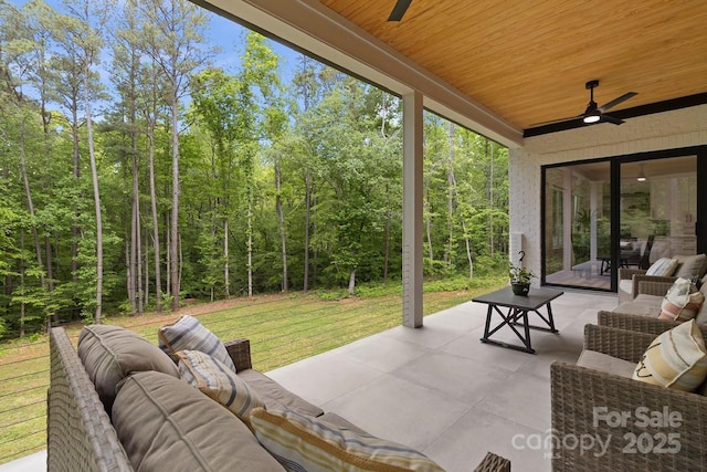 view of patio / terrace featuring an outdoor living space, ceiling fan, and a forest view