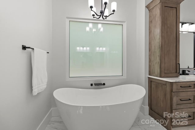 full bath featuring baseboards, a notable chandelier, a freestanding tub, and marble finish floor