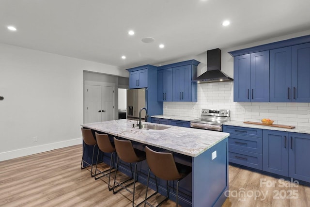kitchen with a sink, appliances with stainless steel finishes, wall chimney range hood, and blue cabinetry