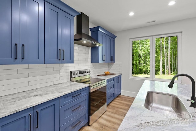 kitchen featuring wall chimney range hood, electric range, blue cabinetry, and a sink