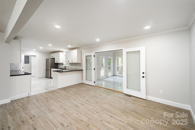 unfurnished living room featuring crown molding, baseboards, french doors, a sink, and light wood-style flooring