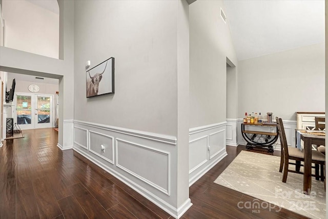 corridor featuring dark wood finished floors, wainscoting, high vaulted ceiling, and french doors