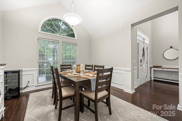 dining room with vaulted ceiling, hardwood / wood-style flooring, wainscoting, and a decorative wall