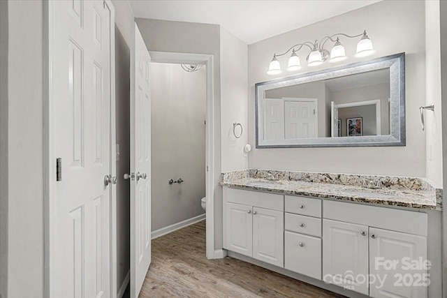 bathroom with wood finished floors, toilet, double vanity, and baseboards