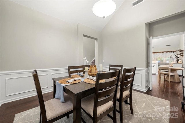 dining space with wood finished floors, lofted ceiling, a wainscoted wall, a decorative wall, and stairs