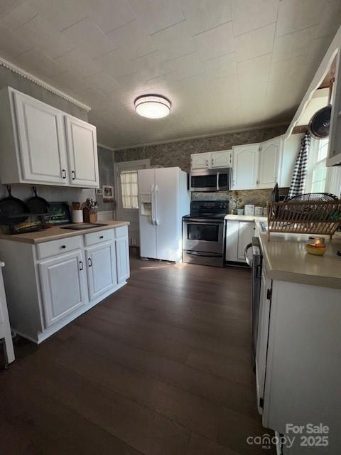 kitchen with dark wood-style floors, light countertops, white cabinetry, a sink, and appliances with stainless steel finishes