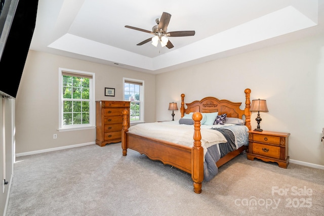 carpeted bedroom with baseboards, a raised ceiling, and ceiling fan