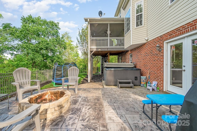 view of patio featuring a sunroom, a hot tub, fence, and a fire pit