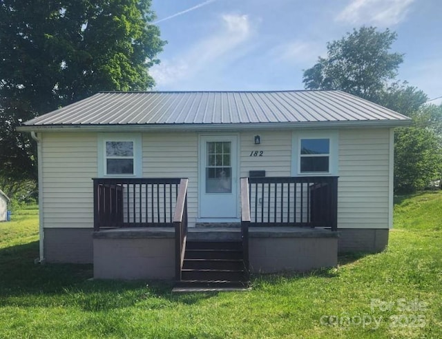 rear view of property featuring a lawn and metal roof
