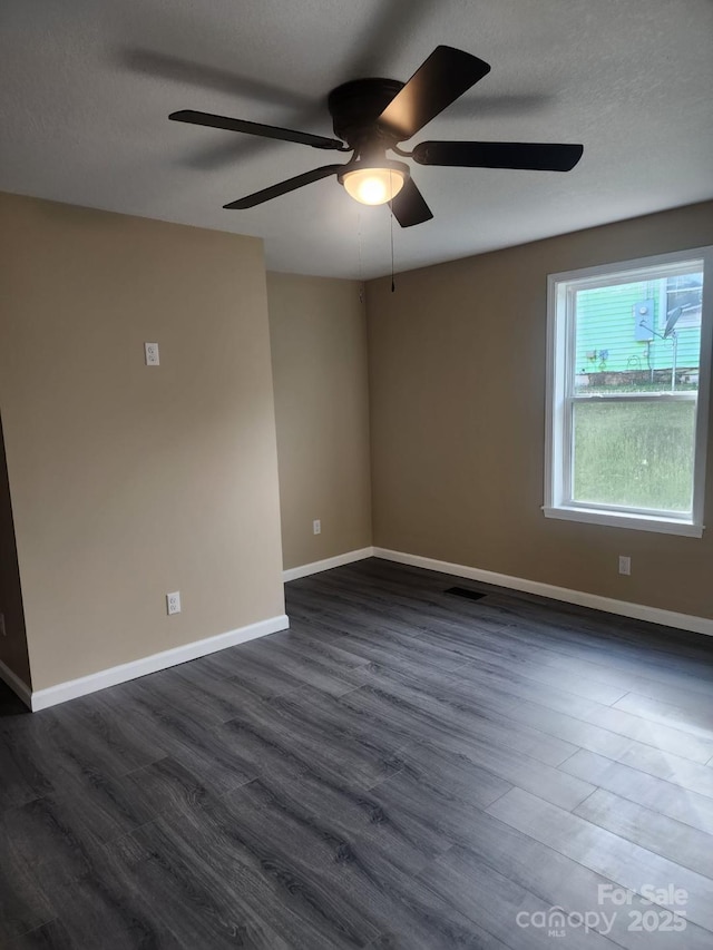 empty room with a textured ceiling, a ceiling fan, baseboards, visible vents, and dark wood-style floors