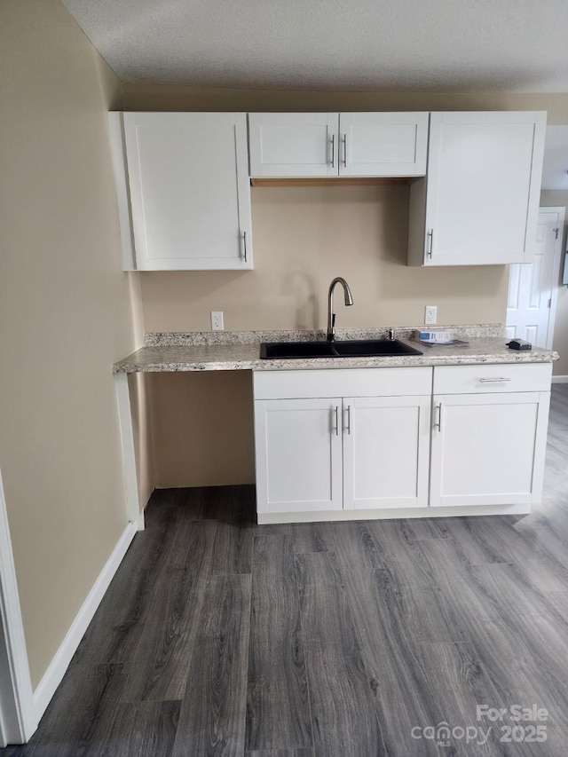 kitchen featuring a sink, light stone countertops, dark wood-style flooring, and white cabinetry