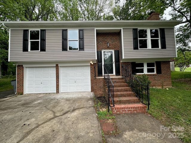 raised ranch with a chimney, an attached garage, driveway, and brick siding