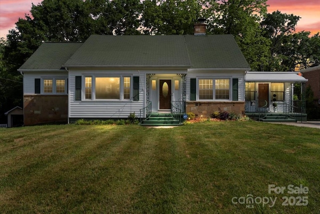 view of front of property featuring a yard, a porch, a chimney, and stone siding