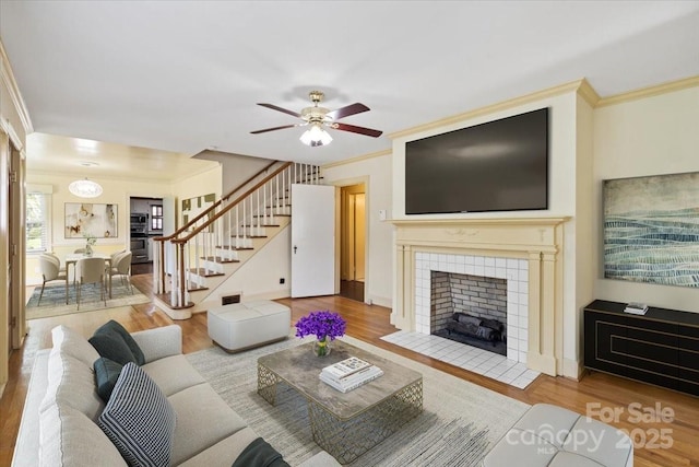 living area featuring ceiling fan, ornamental molding, wood finished floors, and stairway