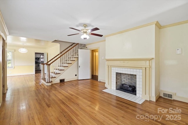unfurnished living room with visible vents, ceiling fan, stairway, a tile fireplace, and light wood-style flooring
