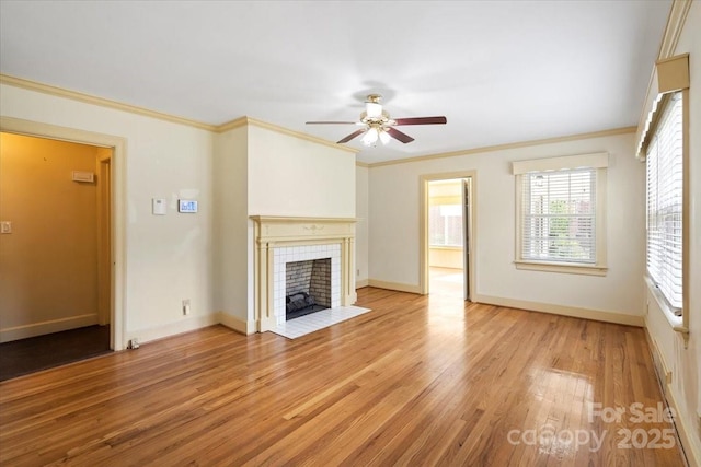 unfurnished living room with a tiled fireplace, crown molding, light wood finished floors, and ceiling fan