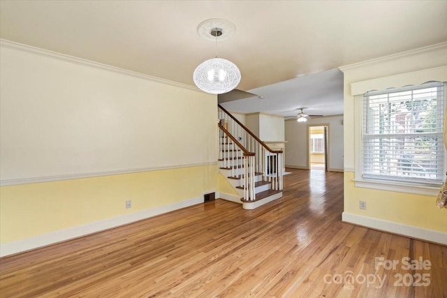 unfurnished room with ceiling fan with notable chandelier, baseboards, wood finished floors, ornamental molding, and stairway