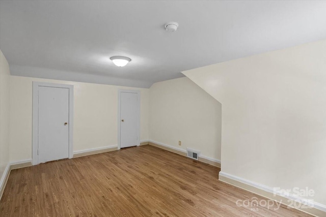 additional living space featuring baseboards, lofted ceiling, wood finished floors, and visible vents