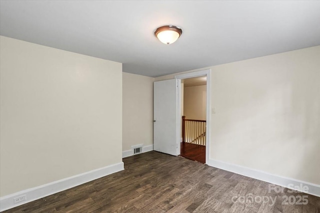 unfurnished room with baseboards, dark wood finished floors, and visible vents