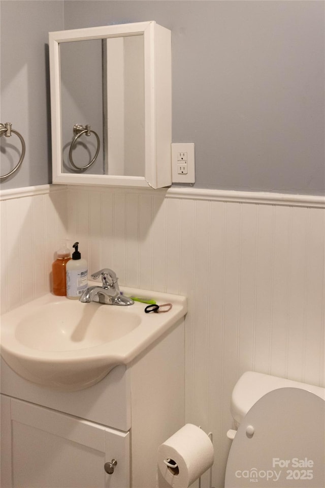 half bath with toilet, wainscoting, and vanity