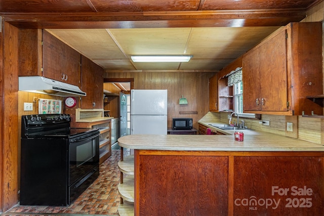 kitchen with wood walls, a sink, black appliances, brick patterned floor, and under cabinet range hood