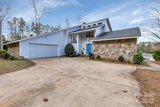 mid-century modern home featuring concrete driveway, stone siding, and a garage