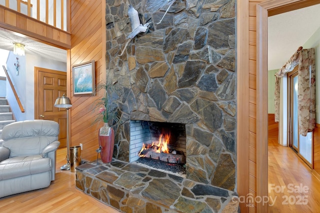 living area featuring stairway, wood walls, a stone fireplace, and wood finished floors