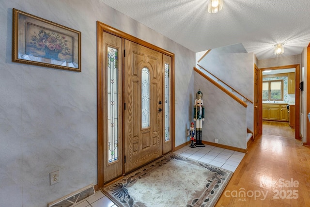 entrance foyer featuring a textured ceiling, light wood-type flooring, visible vents, stairway, and baseboards