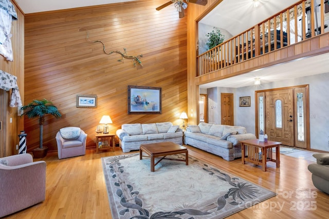 living room featuring wooden walls, wood finished floors, a ceiling fan, and a high ceiling
