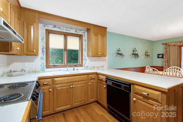 kitchen with a sink, a peninsula, stainless steel range with electric stovetop, black dishwasher, and under cabinet range hood
