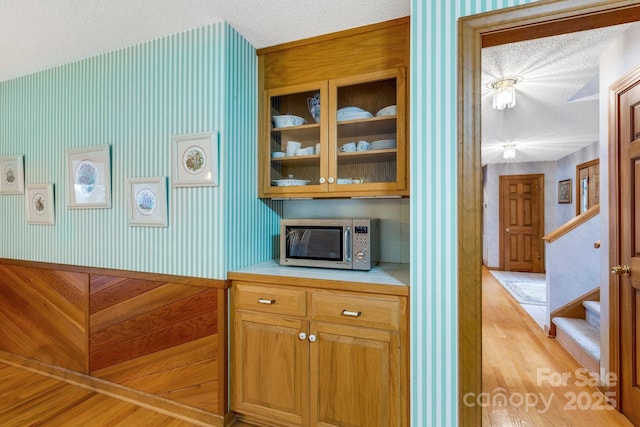 kitchen featuring a textured ceiling, glass insert cabinets, stainless steel microwave, and light wood-style flooring