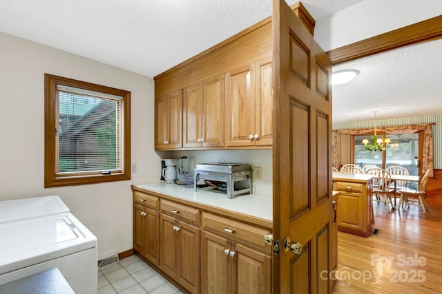 clothes washing area with cabinet space, washer and clothes dryer, a notable chandelier, and a textured ceiling