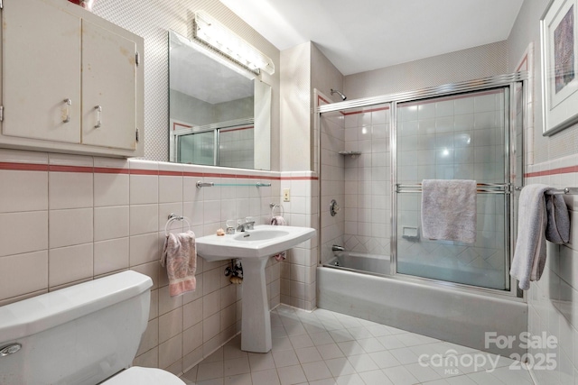 bathroom with tile walls, enclosed tub / shower combo, toilet, a sink, and tile patterned floors