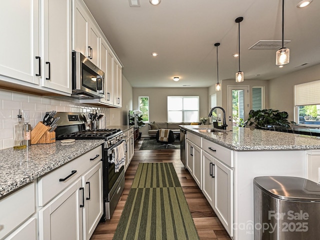 kitchen with a sink, dark wood-style flooring, open floor plan, and appliances with stainless steel finishes