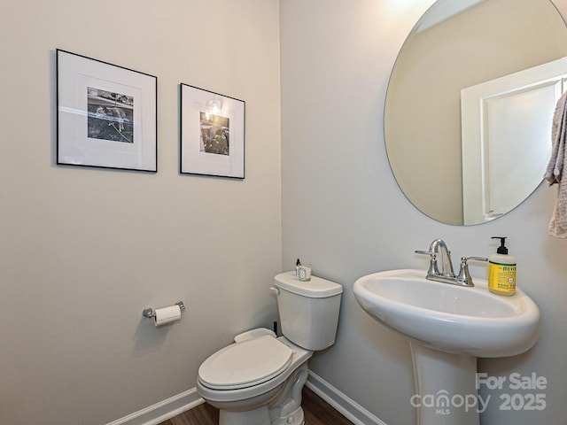 half bath with baseboards, toilet, and wood finished floors