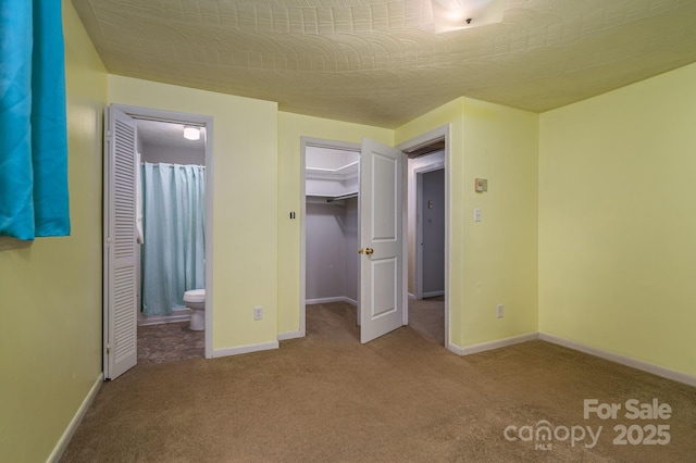 unfurnished bedroom with carpet floors, baseboards, a closet, a spacious closet, and ensuite bathroom