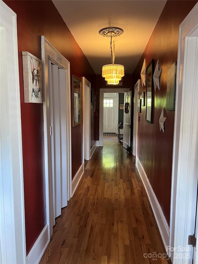 hall featuring baseboards, dark wood-style flooring, and a notable chandelier