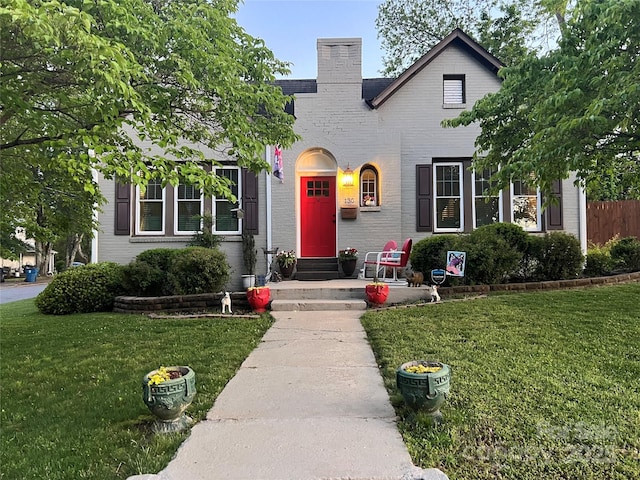 english style home with brick siding, a front lawn, a chimney, and entry steps