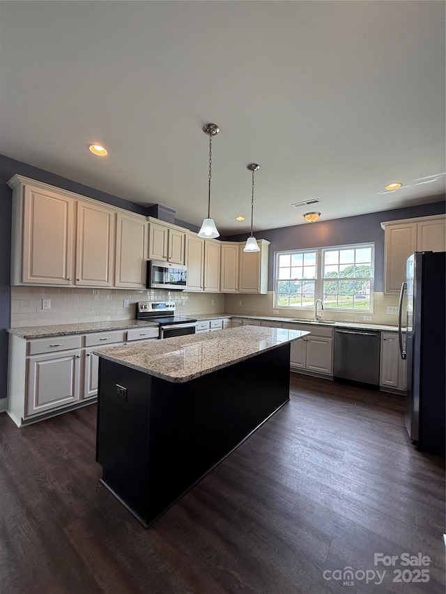 kitchen with dark wood-style flooring, a center island, stainless steel appliances, decorative light fixtures, and backsplash