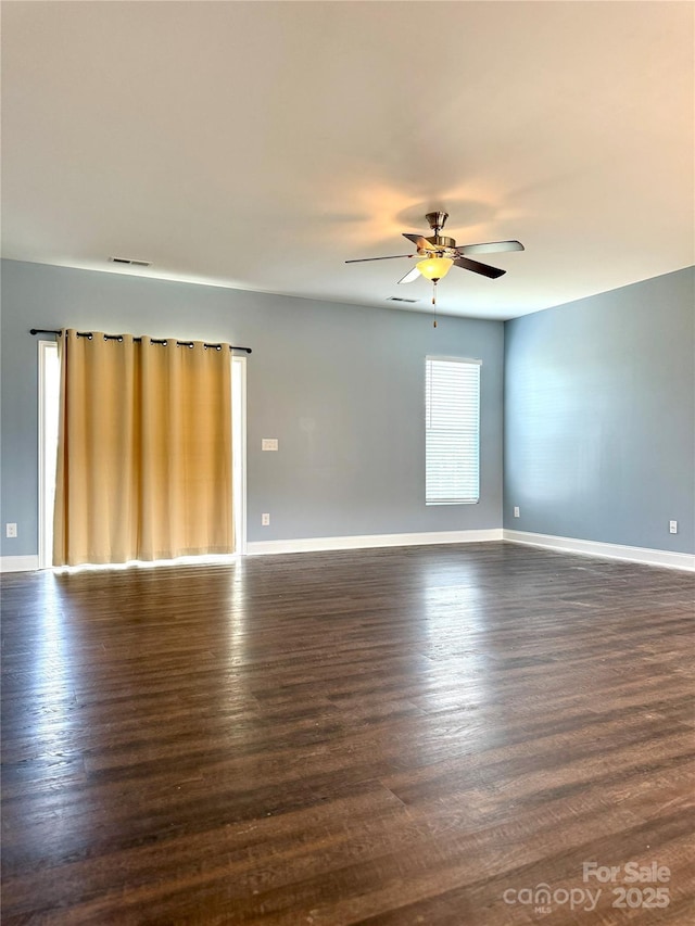 unfurnished room with baseboards, ceiling fan, dark wood finished floors, and visible vents