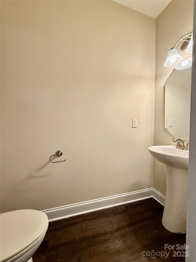 bathroom featuring baseboards, a sink, wood finished floors, and toilet