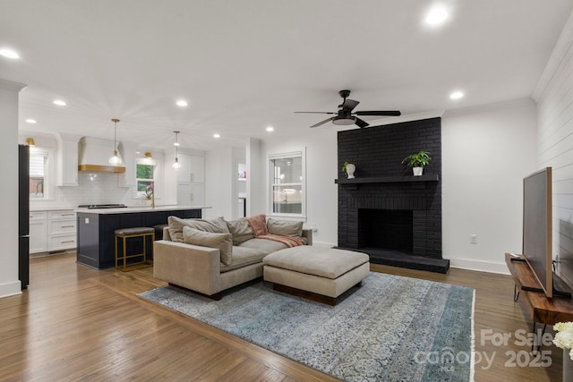 living area with ceiling fan, recessed lighting, a brick fireplace, dark wood-style flooring, and crown molding