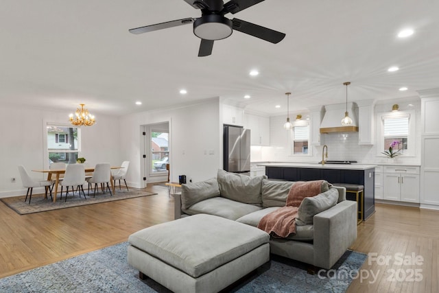 living room featuring light wood-style floors, a chandelier, plenty of natural light, crown molding, and recessed lighting