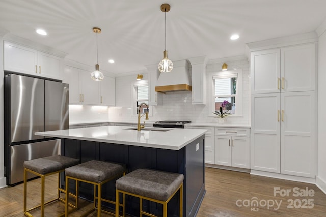 kitchen featuring freestanding refrigerator, premium range hood, a sink, healthy amount of natural light, and recessed lighting