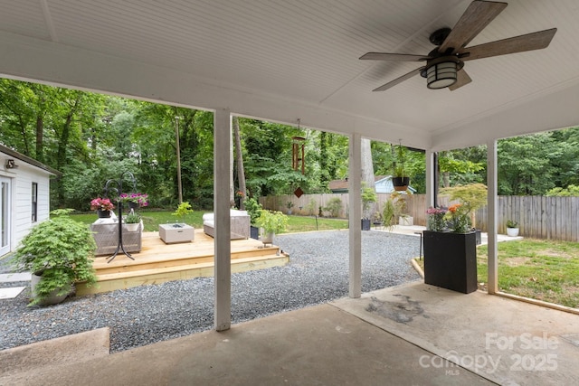 view of patio featuring a wooden deck, a fenced backyard, a ceiling fan, and view of scattered trees
