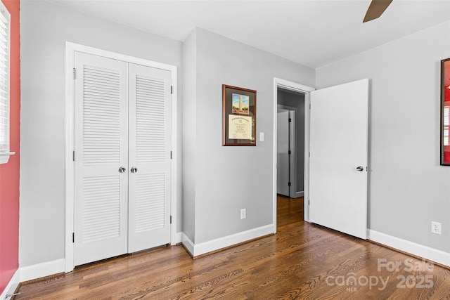 unfurnished bedroom with wood finished floors, a closet, baseboards, and a ceiling fan